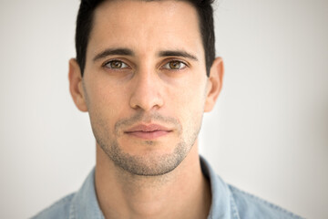 Obraz premium Serious attractive brunette Latin man looking at camera posing for close facial shot. Handsome black haired 20s Hispanic model guy with stubble close up cropped close up front portrait