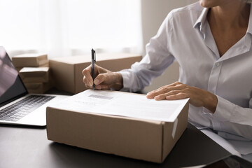 Warehouse worker sit at desk, holds pen, writing shipping address on delivery box, preparing...