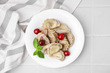 Traditional Ukrainian dumplings (varenyky) with cherries on white tiled table, top view