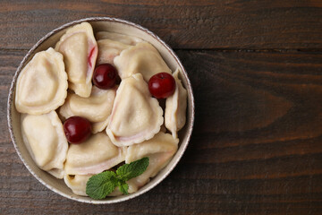 Traditional Ukrainian dumplings (varenyky) with cherries on wooden table, top view. Space for text