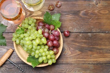 Fresh ripe grapes and glasses of wine on wooden table, flat lay. Space for text