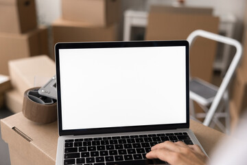 Female working on laptop with white mock up in stockroom filled with stacked boxes. Electronic...