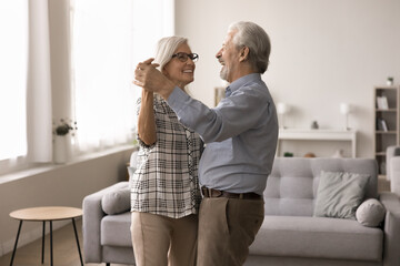 Mature couple in love holding hands moving dancing in modern living room, enjoy romantic dating,...