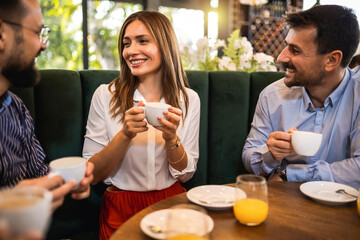 Group of friends hanging out at the restaurant. They laugh, talk and drink coffee.