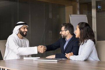 Positive Latin couple of customer consulting Arabian salesman, agent, shaking hands with young Arab...