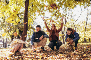 Happy family throwing colorful autumn leaves in the park.