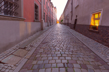 A deserted narrow cobblestone street in the center of Poznan at dawn.