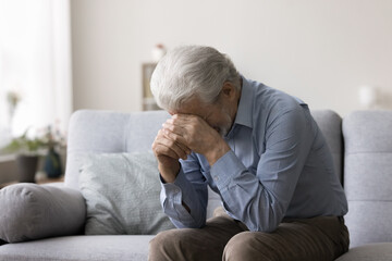 Depressed older retired man sit on sofa, crying, covering face with hands, feeling deep desperation, experiencing grief, loved one death, bad news, suffer from loneliness. Disorder, depression, loss