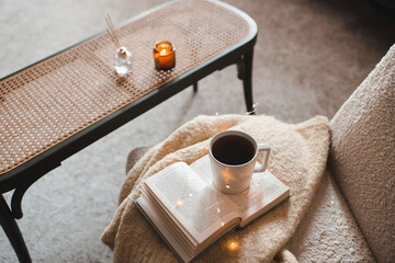 Cup of coffee staying on open paper book and knitted sweater on chair close up. Autumn or winter...