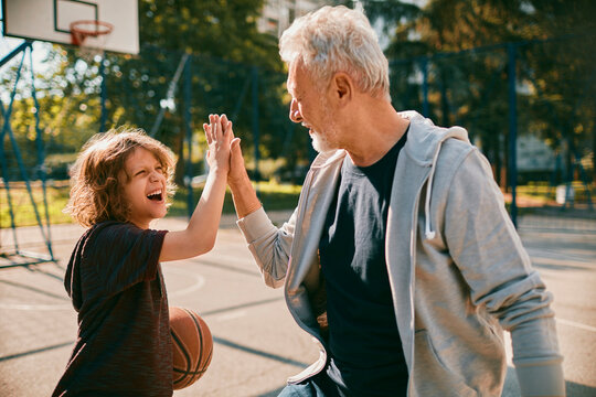 Grandfather and grandson high-five after playing basketball at outdoor court