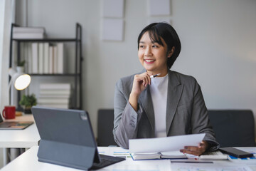 Young businesswoman is holding a pen and thinking about new business strategies while working in an office