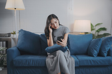 Young asian woman sitting on a sofa is feeling stressed while using a smartphone at home