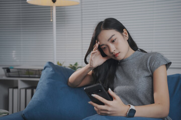 Obraz premium Young woman is sitting on her couch, feeling stressed while using her smartphone at home