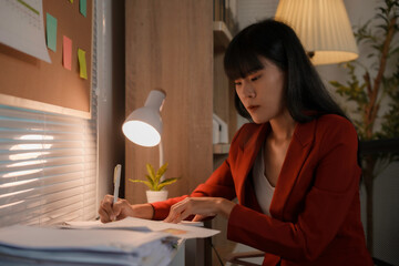 Businesswoman is working late at night, using a desk lamp to illuminate her paperwork