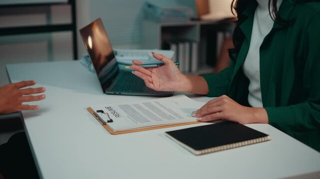 Businesswoman sitting at her desk explains contract terms to her partner, facilitating understanding before signing a business agreement. Collaboration and communication are key