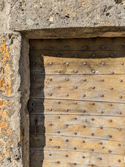 Close-Up of a Rustic Wooden Door with Weathered Metal Rivets Framed by Textured Grunge Stone, Perfect for Vintage Backgrounds, Architectural Details, and Projects Requiring Depth and Rustic Charm