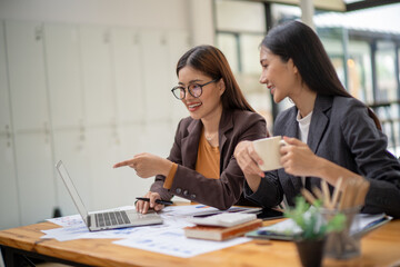 Two women are sitting at a desk with a laptop and a cup of coffee