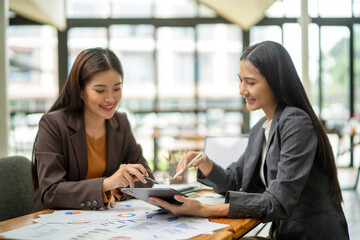 Two women are sitting at a table, one of them pointing at a tablet