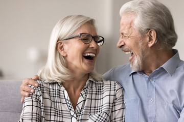 Close up laughing overjoyed older spouses sit on sofa telling anecdotes and jokes, having fun while talking on pastime at home. Cherished memories, harmonious relationship after many years together