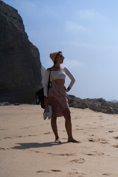 Young woman on cliff looking out over ocean in summer in Portugal.
