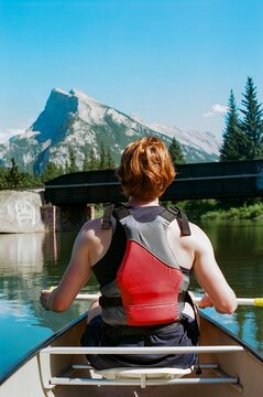 Person rowing a canoe on calm waters with a mountain backdrop
