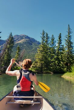 A person paddles through a tranquil lake surrounded by lush trees