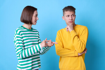 Emotional young couple having quarrel on light blue background
