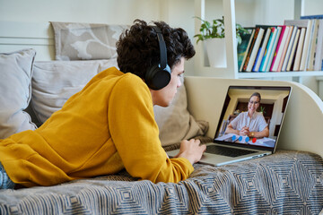 Young male patient having online meeting with psychologist, lying on couch