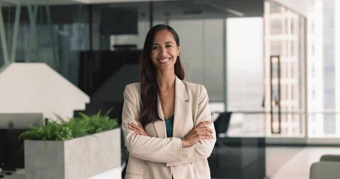 Attractive smiling confident businesslady standing with arms-crossed in modern workspace. Portrait of company executive manager, looking at camera at workplace. Professionalism, business owner shot