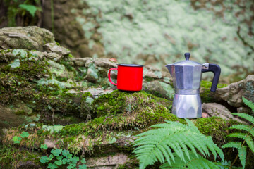 Coffee pot and metal cup on a large stone against the background of a mountain river. Coffee pot on...