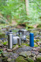 Coffee pot and metal cup on a large stone against the background of a mountain river. Coffee pot on...