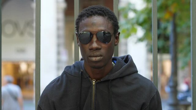 young african migrant wearing sunglasses stares seriously at the camera