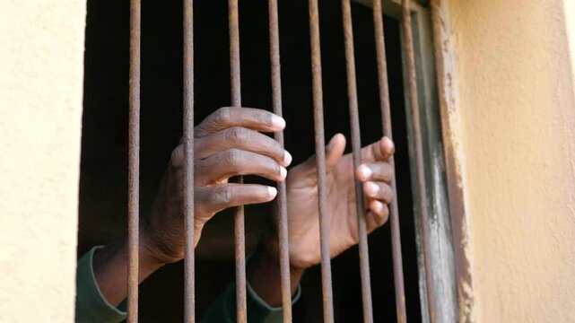 imprisonment symbol - hands of black man grab the bars of the window