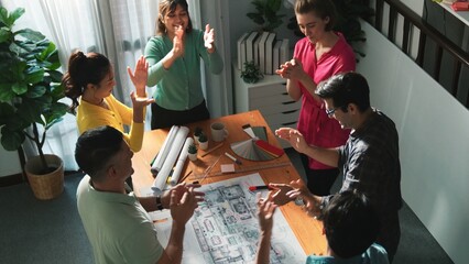 Top view of smart civil engineer team clapping hand while discussing idea at meeting table with blueprint, color palette and equipment. Top aerial view of diverse people clap hand. Unity. Symposium.