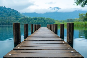 Fototapeta premium A serene wooden dock leads out into a calm lake with mountains in the background.