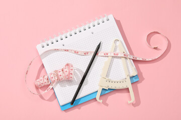 Body fat caliper, measuring tape, notebook and pencil on pink background, flat lay