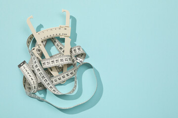 Plastic body fat caliper and measuring tape on light blue background, top view. Space for text