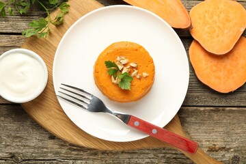 Tasty mashed sweet potato, parsley and walnuts served with sauce on wooden table, flat lay