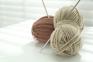 Skeins of soft yarn and knitting needles on white table indoors, closeup. Space for text