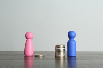 Financial inequality. Male and female figures with uneven amount of coins on wooden table