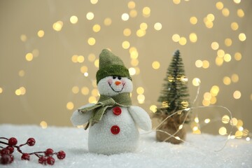Cute decorative snowman and other Christmas decor on artificial snow against blurred lights