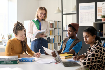Portrait of female teacher working in class with group of college students sitting at table with...