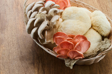 A wicker basket displaying various exotic mushrooms including lion's mane and pink oyster mushrooms.