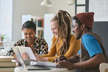 Multiethnic group of students using digital tablet while studying with online resources at table...