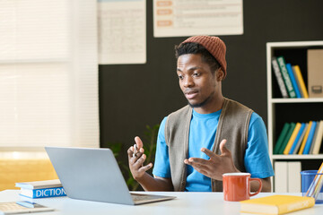 Black young man as student discussing topic during video call with online tutor while sitting at...