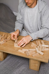 person stacks wooden blocks to construct tower on table in a room, Man playing table game for concentration at home. Digital detox