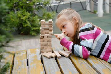 Person stacking wooden blocks, building tower while seated at a table outdoors, concentrating on...