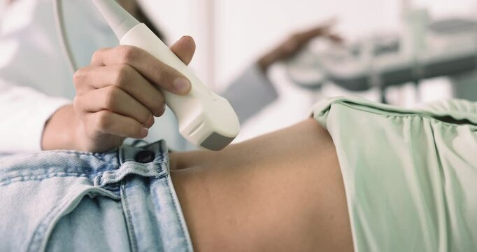 Female pass abdominal or gynecological ultrasound examination in clinic, close up. Sonographer or ultrasound technician check patient internal organs using convex probe and ultrasonography equipment