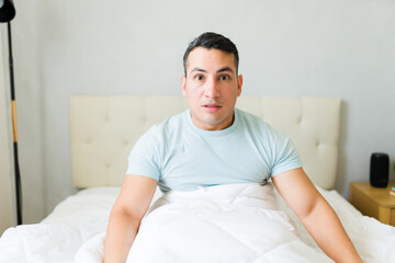 Startled and bewildered young man waking up in his bed in the morning