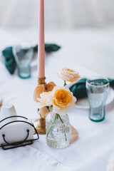 Empty tableware set, candles, white tablecloth, flowers, decorated table with glass crystal stand in restaurant indoor. Photography, design concept for banquet.